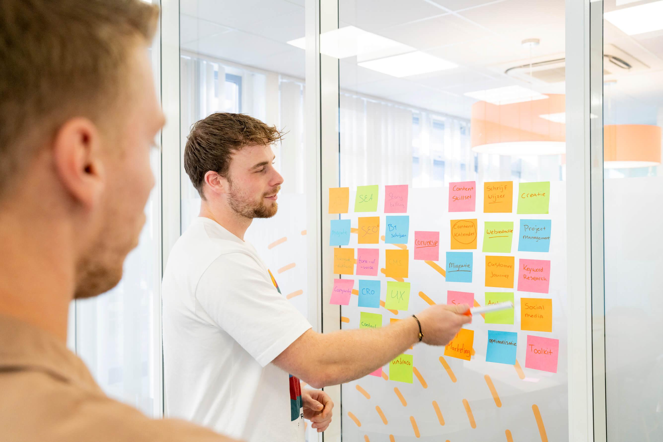 Man wijst naar een muur met post-its tijdens een brainstormsessie