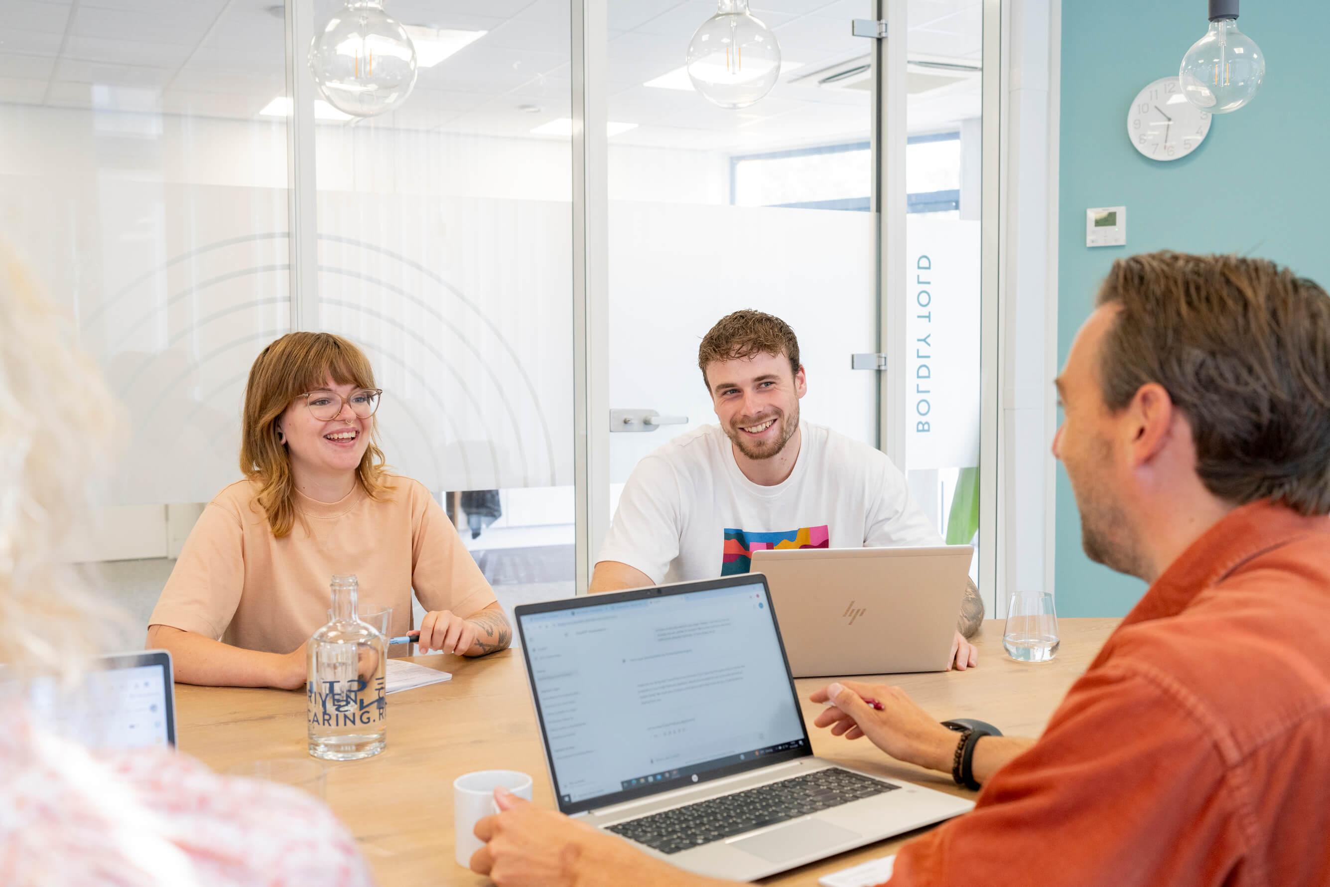 Collega's lachen tijdens een vergadering aan tafel met laptops
