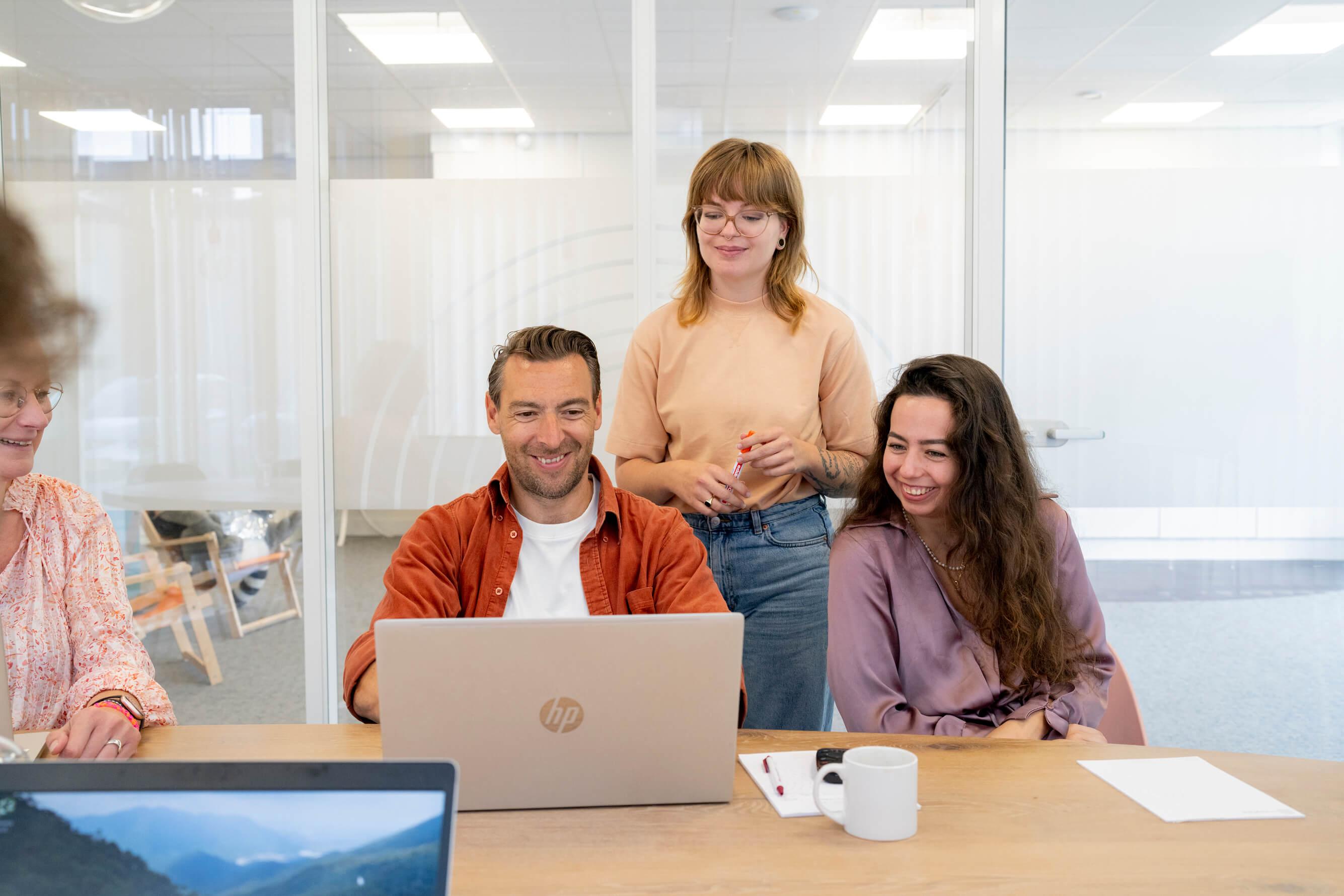 Drie collega's samen rond een laptop in een vergaderruimte