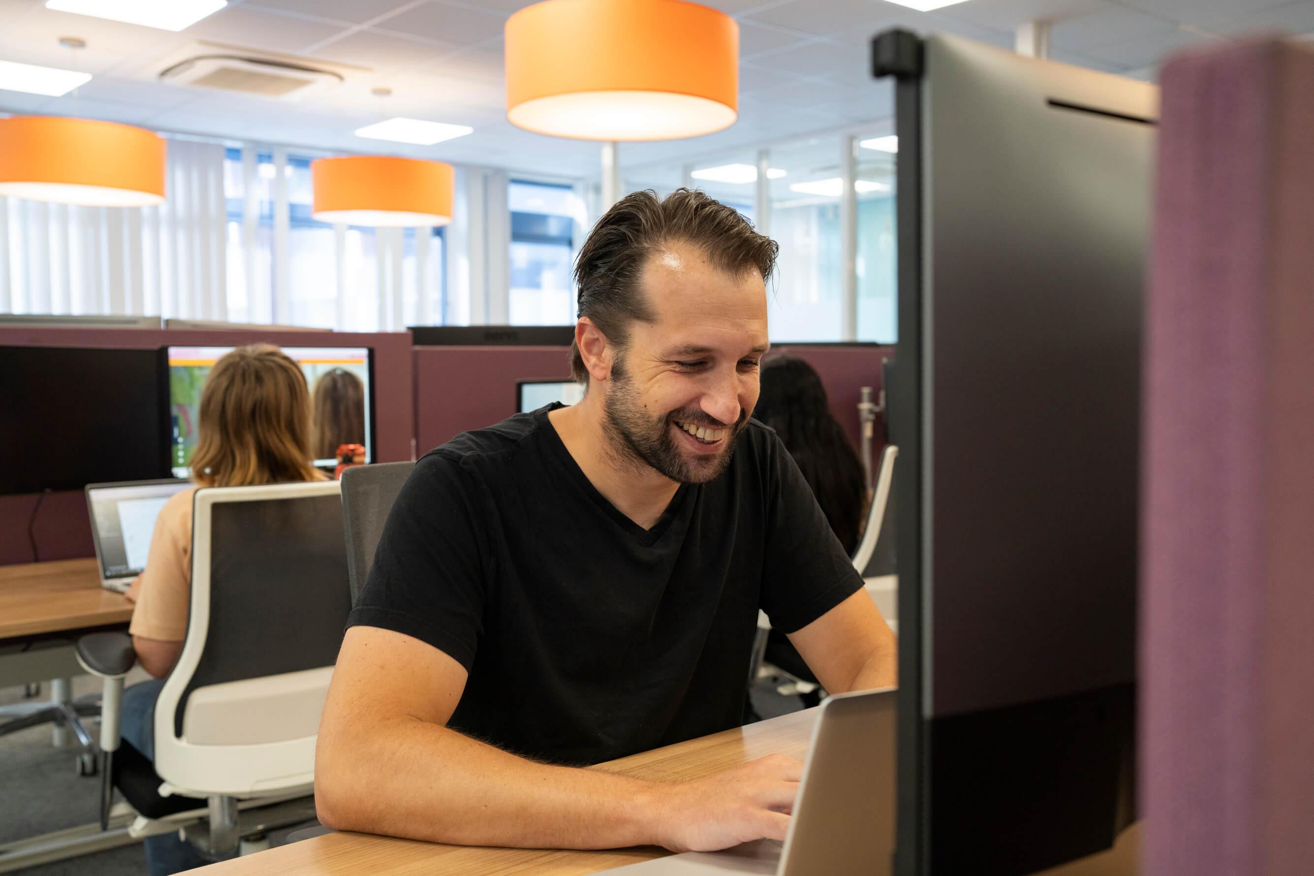 Man glimlacht terwijl hij op een laptop werkt op kantoor
