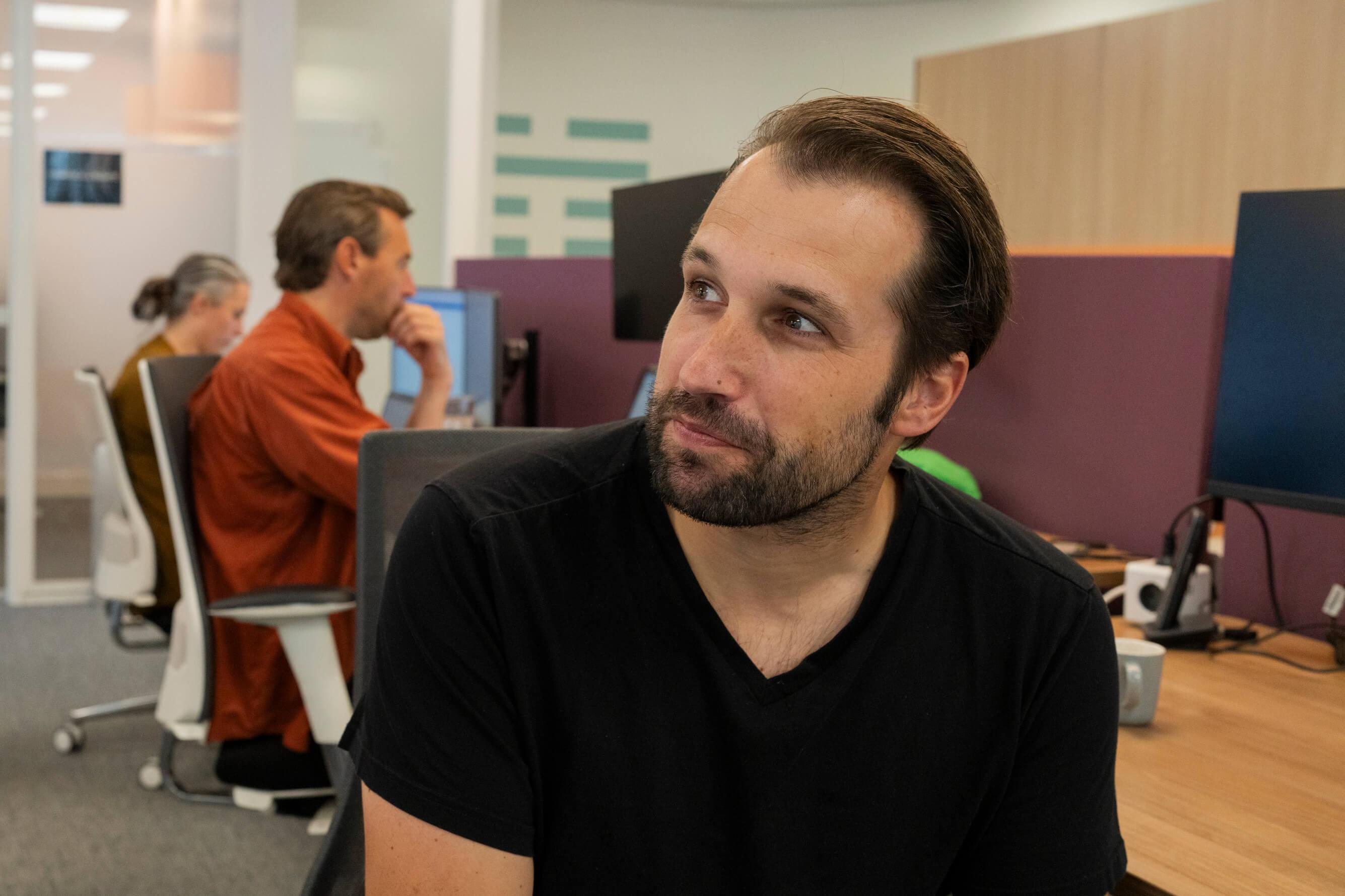 Man kijkt opzij in een kantoor met collega's op de achtergrond