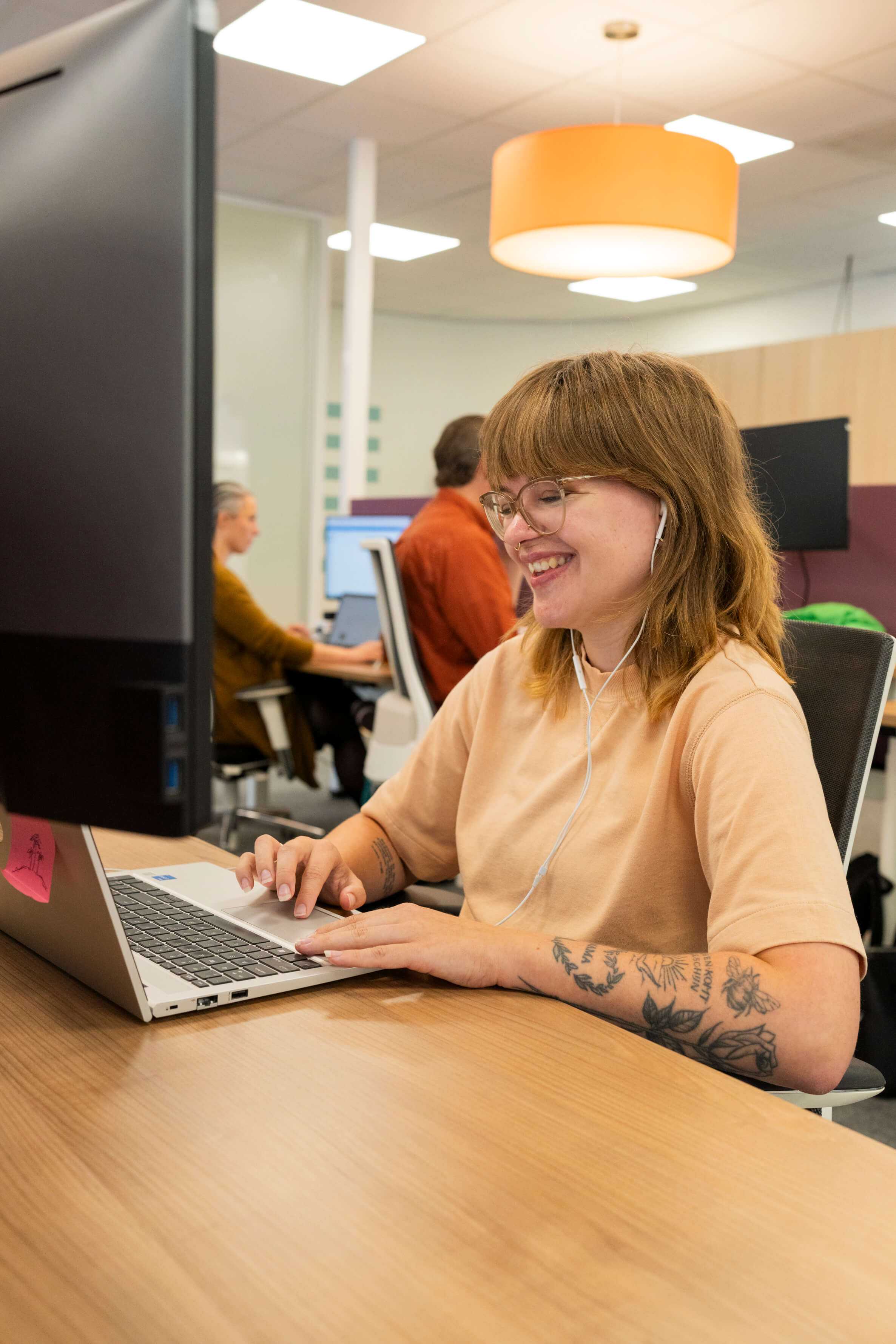 Vrouw glimlacht terwijl ze met oordopjes in werkt op een laptop