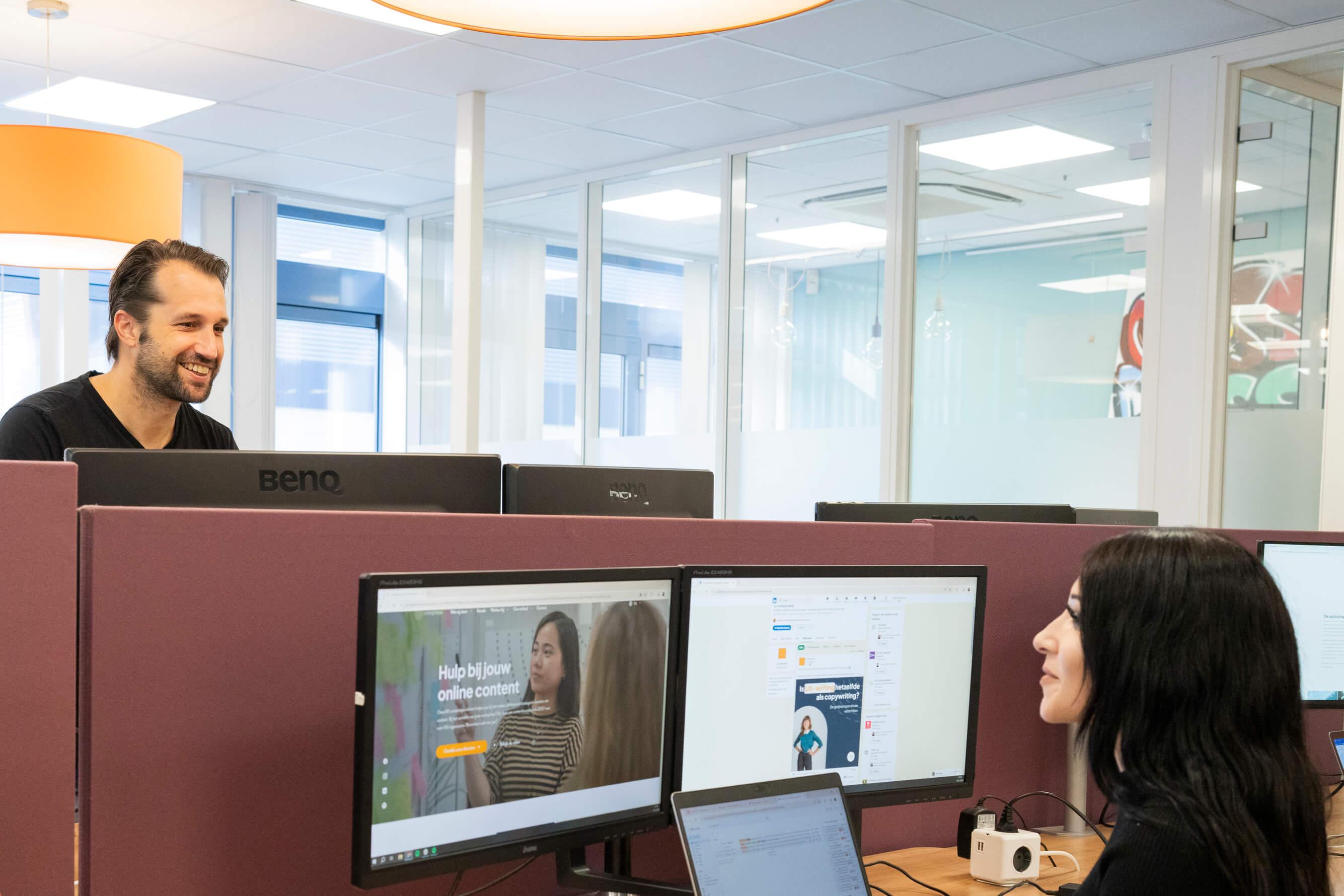 Twee collega's overleggen aan bureau's in een open kantoorruimte